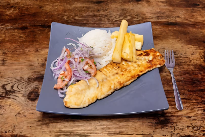 Grilled fish fillet with white rice, yucca fries, and a red onion and tomato salad.