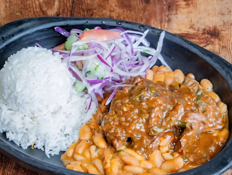 A black bowl filled with white rice, a side salad, and a stew of beans and meat.